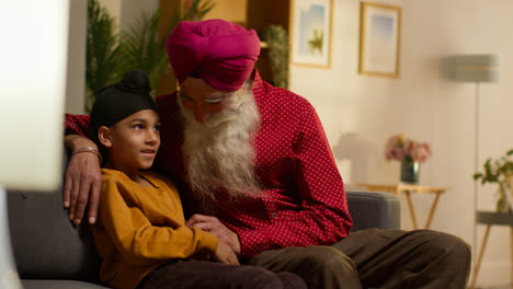 Smiling-Sikh-Grandfather-And-Grandson-Wearing-Turbans-Sitting-On-Sofa-At-Home-Talking-Together-3